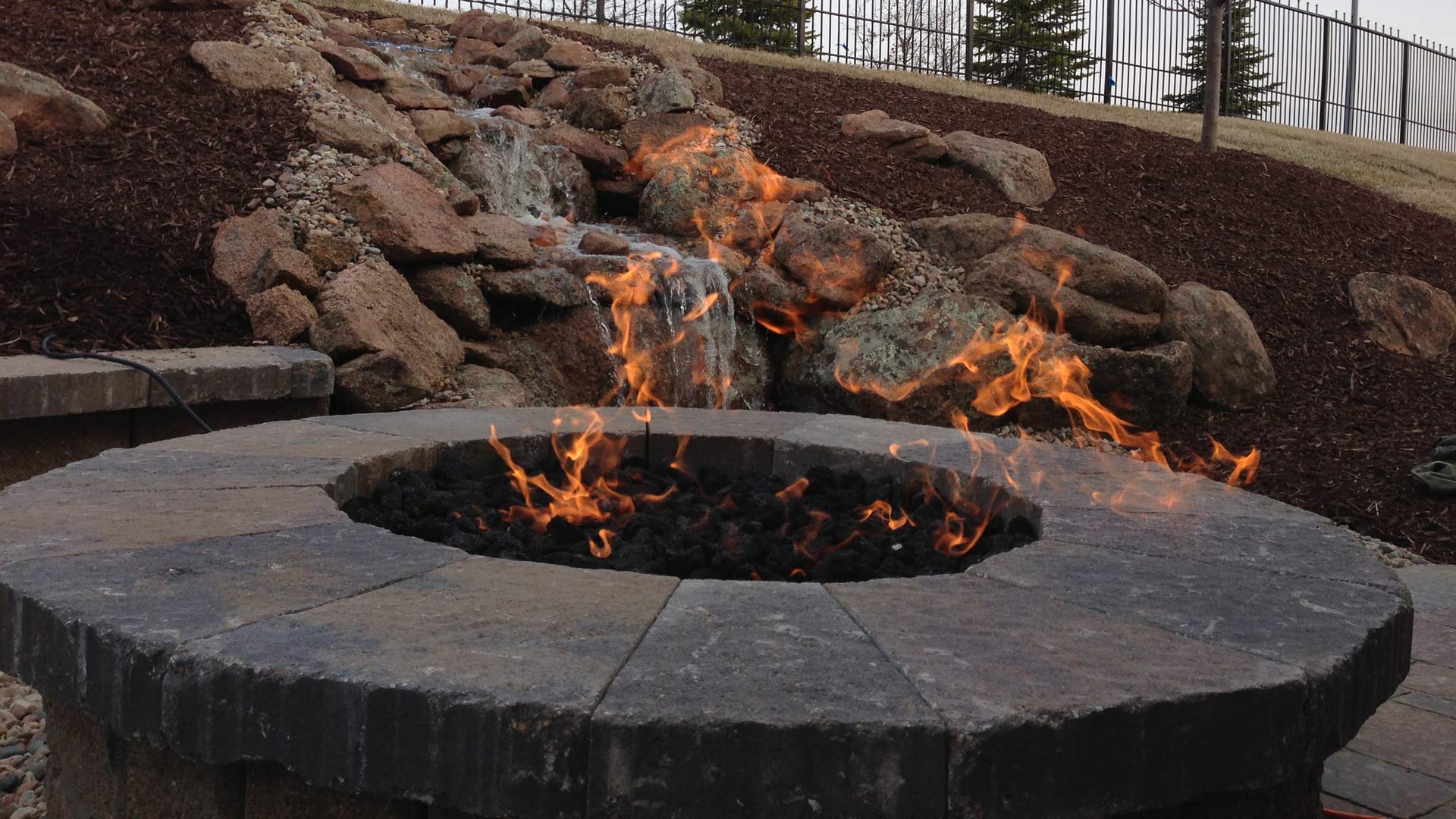 Fire pit flaming with water feature in the background in Valley, NE.
