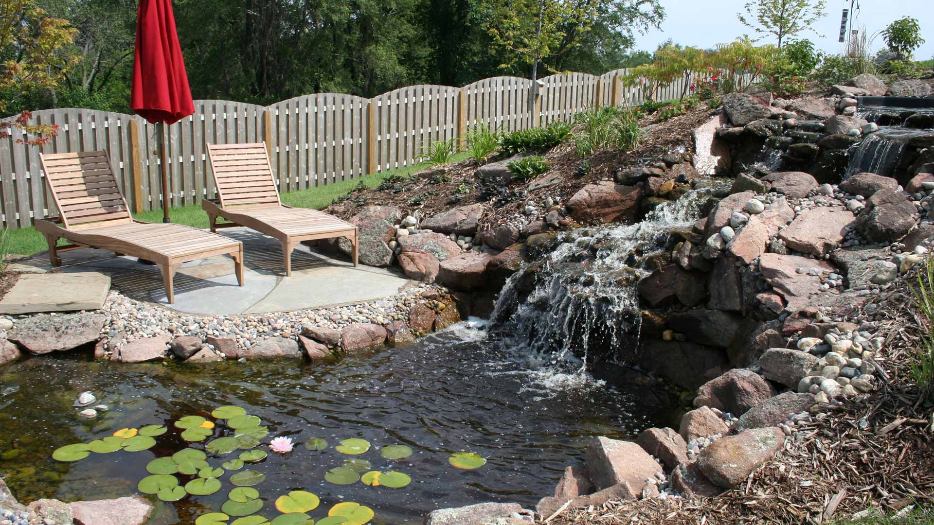 Waterfall hardscape feature installed with patio chairs on platform in Omaha, NE.