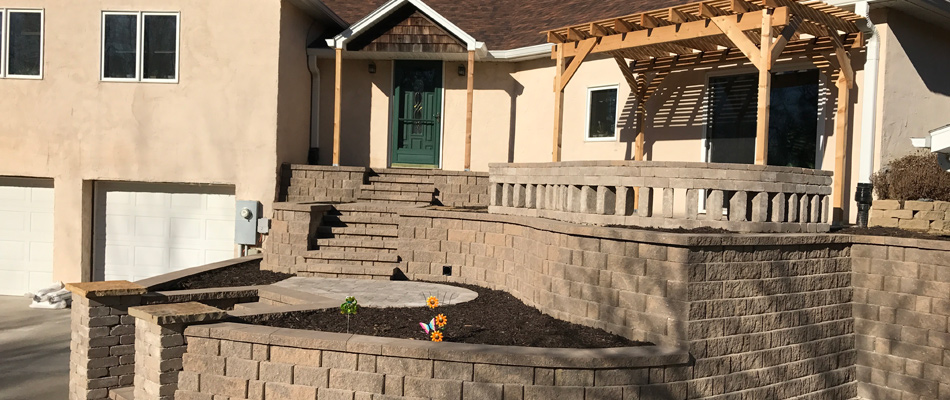 Stone retaining wall built with steps leading up to door with a pergola installed in Omaha, NE.