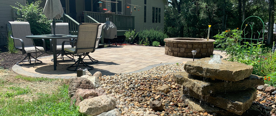 A water feature installed beside a patio with a fire pit in Millard, NE.